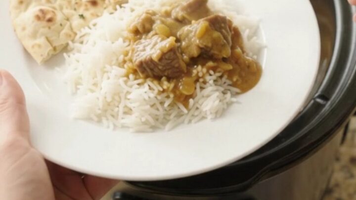 Golden korma beef brisket in a slow cooker, topped with cashew cream and butter pats.