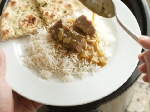Slow cooker garlic butter korma beef brisket in a black ceramic pot, garnished with fresh herbs