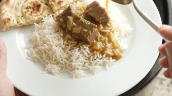 Slow cooker garlic butter korma beef brisket in a black ceramic pot, garnished with fresh herbs