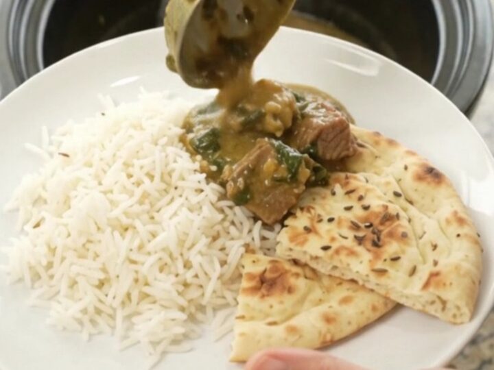 Slow cooker creamy spinach saag beef brisket in a black crock, with steam rising