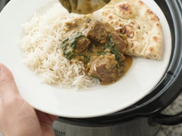 Slow cooker beef brisket saag in a black crockpot, creamy spinach curry with tender beef cubes