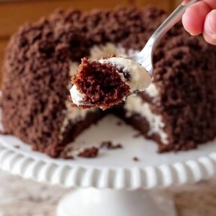 A finished chocolate crumble cake with coconut cream on a white scalloped stand.