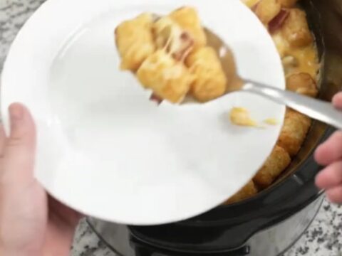 A bubbling Crockpot tater tot bake with melted Colby-Jack cheese and green chiles, served with a spoon.