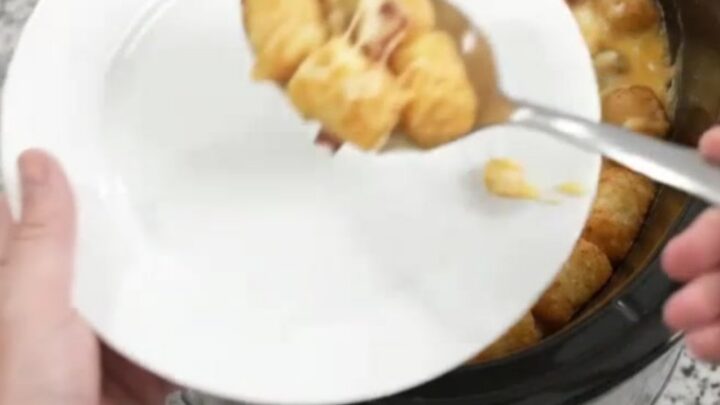 A bubbling Crockpot tater tot bake with melted Colby-Jack cheese and green chiles, served with a spoon.