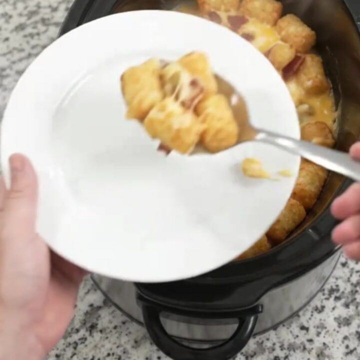 A bubbling Crockpot tater tot bake with melted Colby-Jack cheese and green chiles, served with a spoon.
