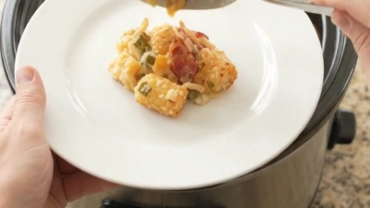 Pepper Jack Green Chile Tater Tot Bake in a black slow cooker, topped with melted cheese and crispy onions.