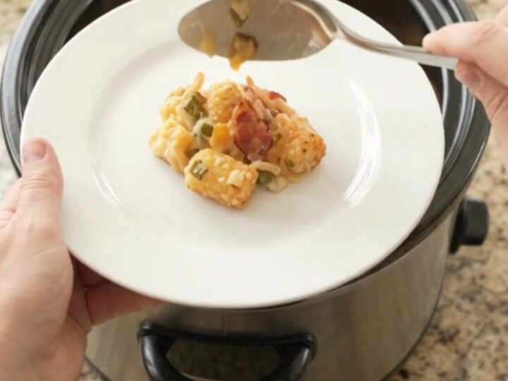 Pepper Jack Green Chile Tater Tot Bake in a black slow cooker, topped with melted cheese and crispy onions.