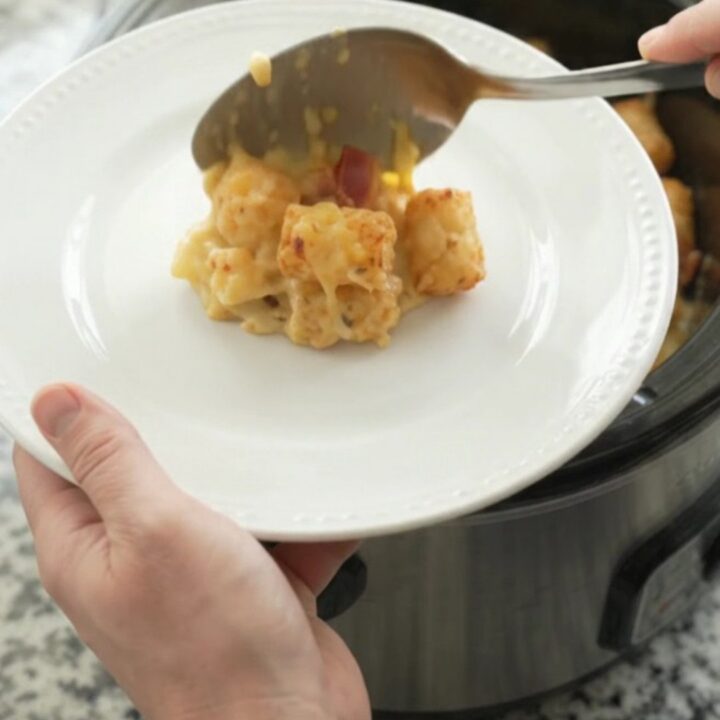 Bubbling smoked gouda broccoli tater tot bake in a black crockpot, with melted cheese and steam rising.