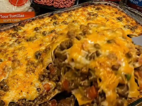 A close-up of a spatula lifting a portion of cheesy, bubbling beef and tortilla casserole from a glass dish.