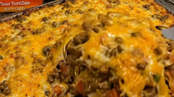 A close-up of a spatula lifting a portion of cheesy, bubbling beef and tortilla casserole from a glass dish.