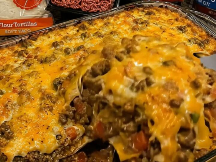 A close-up of a spatula lifting a portion of cheesy, bubbling beef and tortilla casserole from a glass dish.
