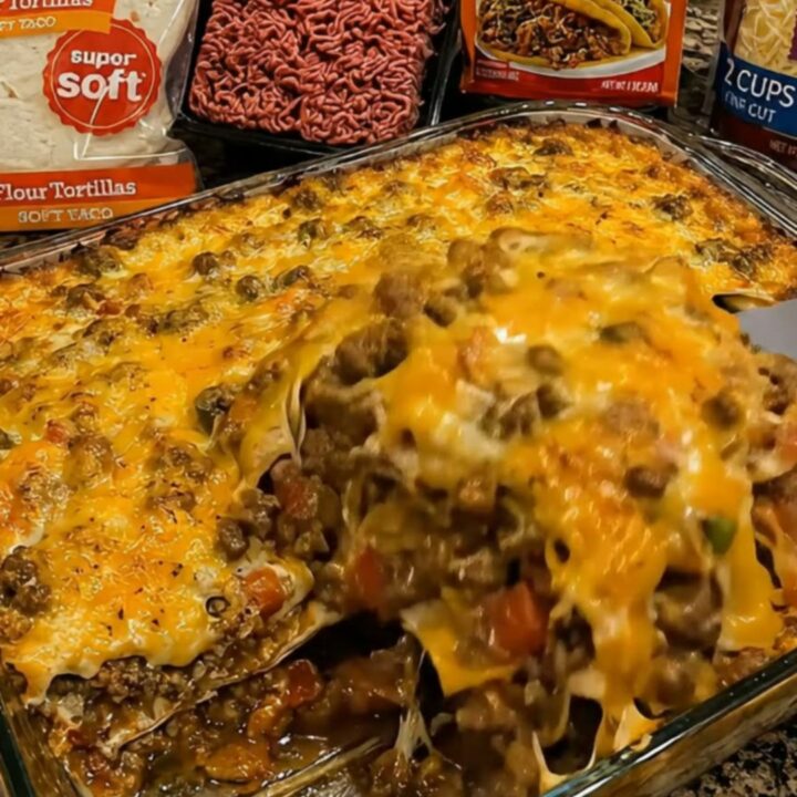 A close-up of a spatula lifting a portion of cheesy, bubbling beef and tortilla casserole from a glass dish.