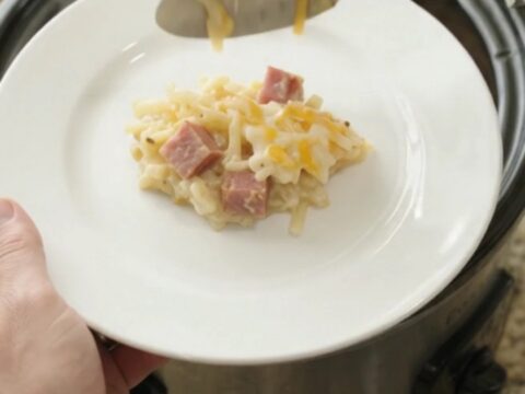 Slow cooker hashbrown casserole with melted cheese and ham, served in a black crockpot