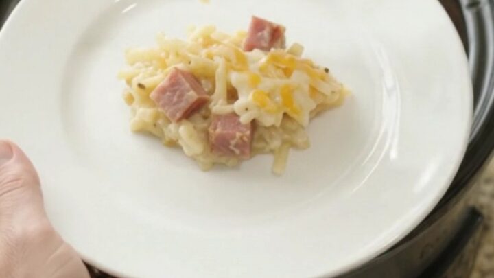 Slow cooker hashbrown casserole with melted cheese and ham, served in a black crockpot