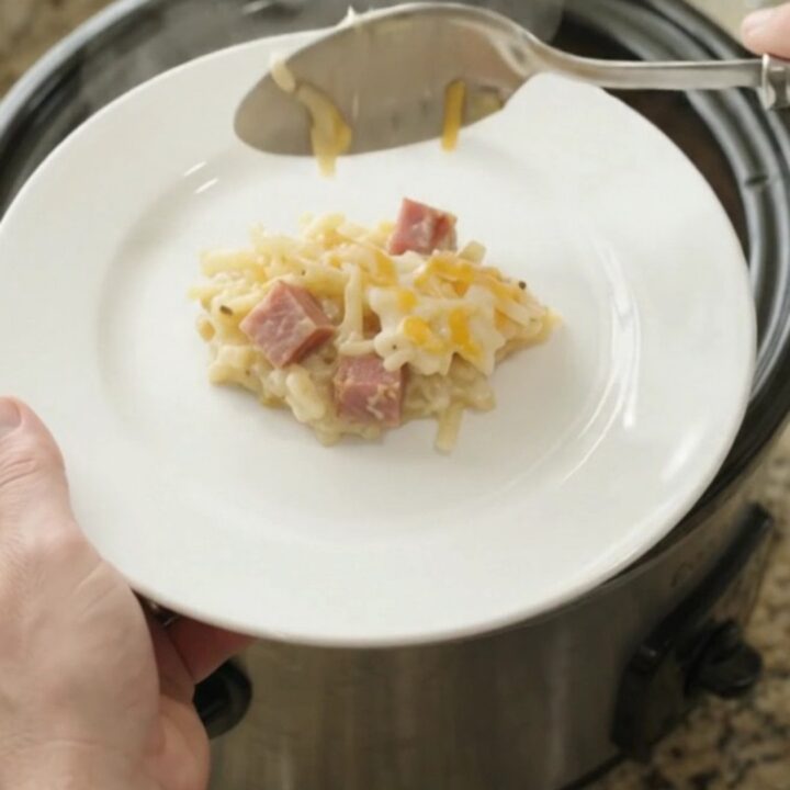 Slow cooker hashbrown casserole with melted cheese and ham, served in a black crockpot