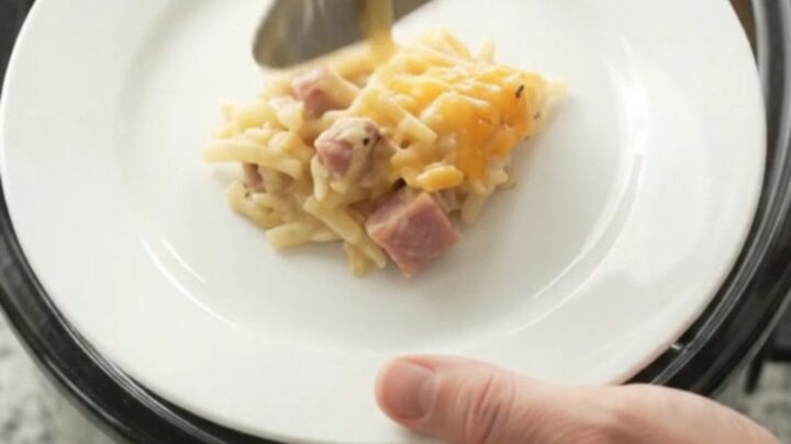 Golden bubbling cheddar hashbrown bake in a black slow cooker, steam rising