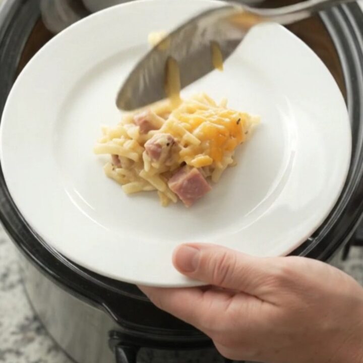 Golden bubbling cheddar hashbrown bake in a black slow cooker, steam rising