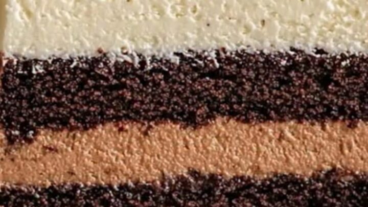 A slice of triple chocolate mousse cake showing distinct layers of white, milk, and dark chocolate with a sponge base.
