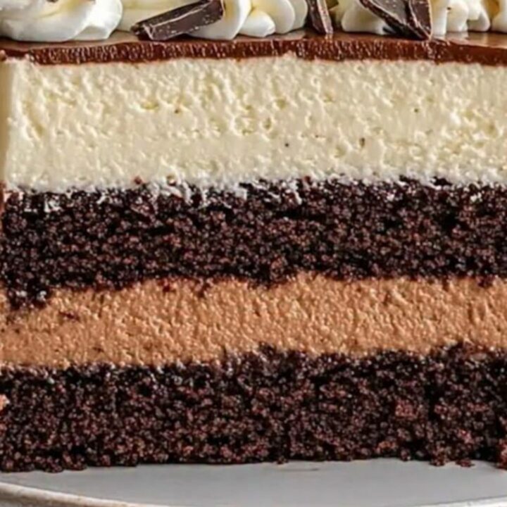 A slice of triple chocolate mousse cake showing distinct layers of white, milk, and dark chocolate with a sponge base.