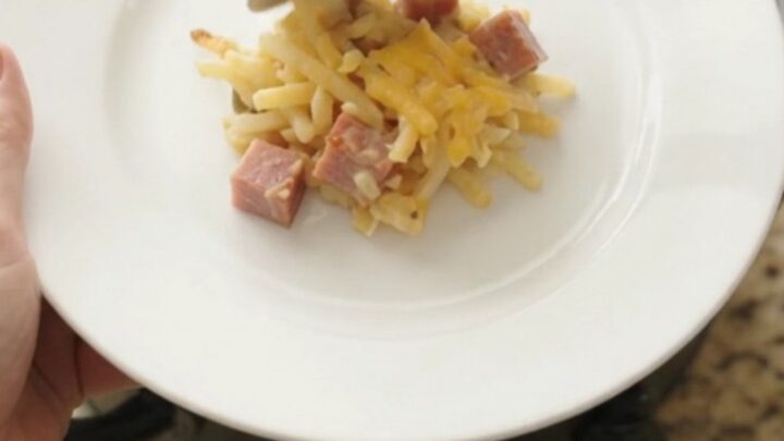 A bubbling slow cooker hashbrown casserole with a golden cheddar crust, topped with melted cheese and butter.