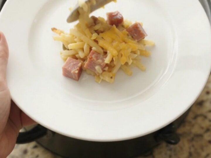 A bubbling slow cooker hashbrown casserole with a golden cheddar crust, topped with melted cheese and butter.