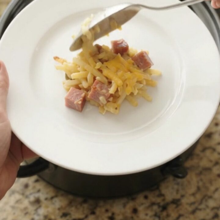 A bubbling slow cooker hashbrown casserole with a golden cheddar crust, topped with melted cheese and butter.