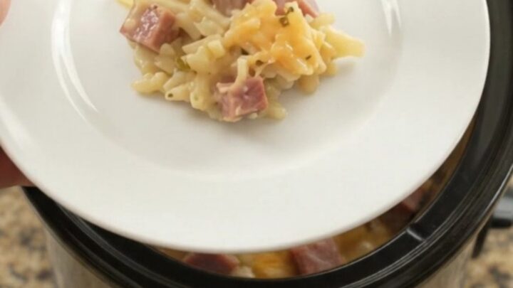 A bubbling slow cooker filled with cheesy hashbrown casserole, topped with melted smoked Gouda and Parmesan