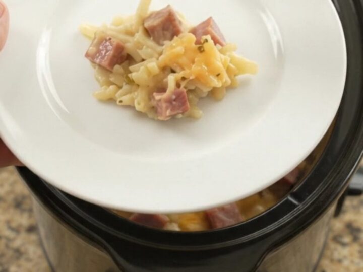 A bubbling slow cooker filled with cheesy hashbrown casserole, topped with melted smoked Gouda and Parmesan