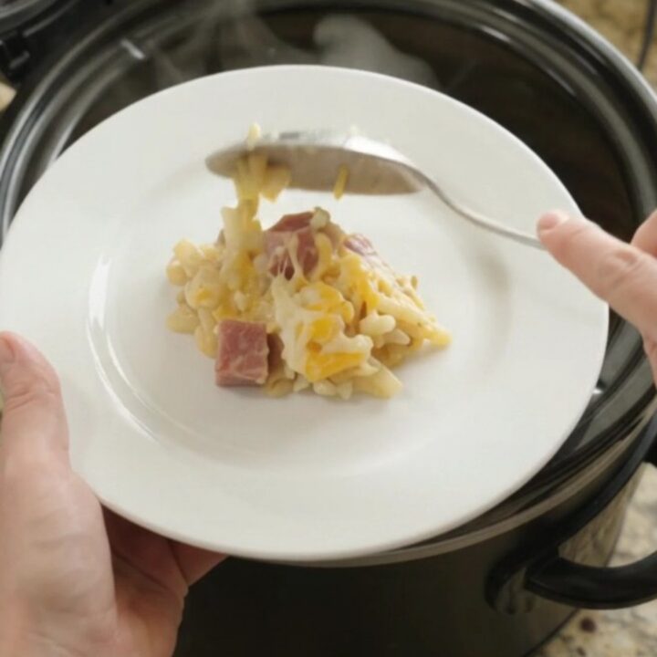 Slow cooker filled with bubbling cheesy hashbrown casserole, topped with melted Colby-Jack and broccoli