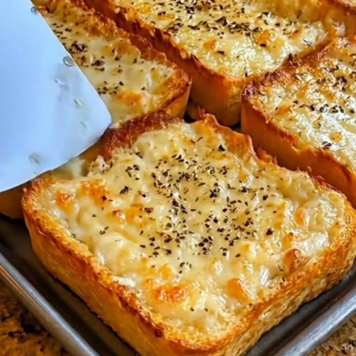 A golden, crispy slice of garlic cheese bread with a long, gooey cheese pull held by a metal spatula.