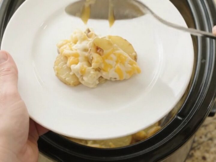 Crockpot full of creamy scalloped potatoes with melted cheese and steam rising