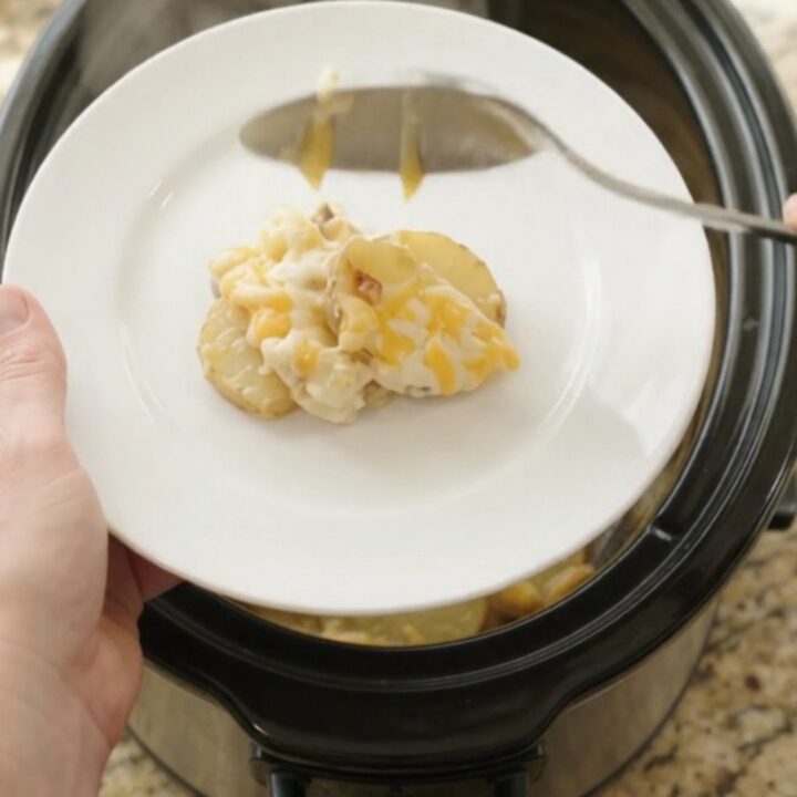 Crockpot full of creamy scalloped potatoes with melted cheese and steam rising