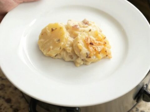 A slow cooker filled with bubbling scalloped potatoes topped with melted pepper jack cheese and crispy onions.