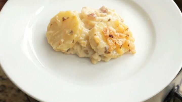 A slow cooker filled with bubbling scalloped potatoes topped with melted pepper jack cheese and crispy onions.