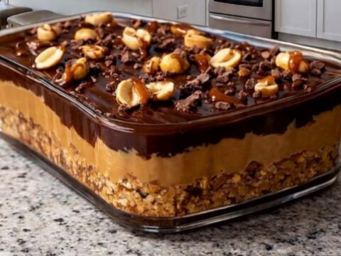 A clear glass dish filled with chocolate caramel peanut bars on a granite countertop, showing distinct layers.