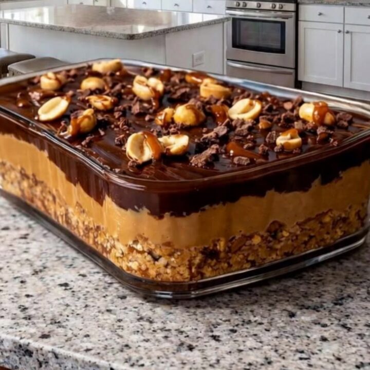 A clear glass dish filled with chocolate caramel peanut bars on a granite countertop, showing distinct layers.