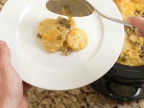 Slow cooker filled with bubbling cheesy scalloped potatoes, topped with golden melted cheddar