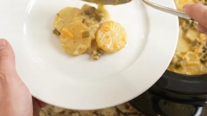 Slow cooker filled with bubbling cheesy scalloped potatoes, topped with golden melted cheddar