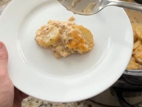 A slow cooker filled with creamy smoked gouda scalloped potatoes, topped with melted cheese and steam rising.