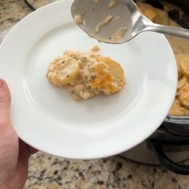 A slow cooker filled with creamy smoked gouda scalloped potatoes, topped with melted cheese and steam rising.