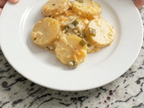 Slow cooker filled with bubbling green chile scalloped potatoes topped with melted Colby-Jack cheese.