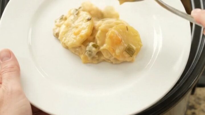 Slow cooker filled with bubbling scalloped potatoes topped with melted smoked Gouda and Parmesan.