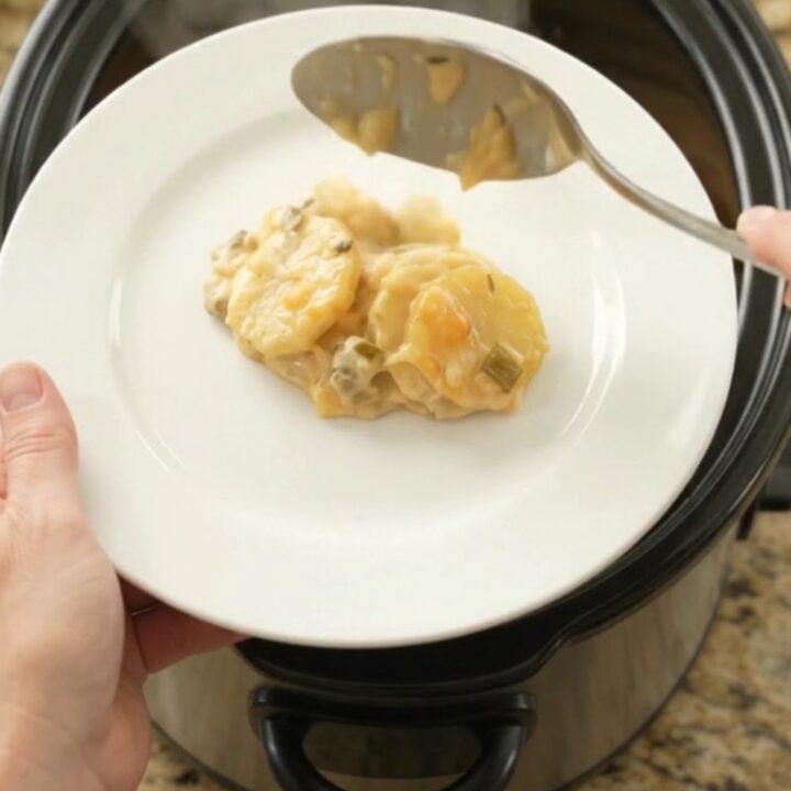 Slow cooker filled with bubbling scalloped potatoes topped with melted smoked Gouda and Parmesan.
