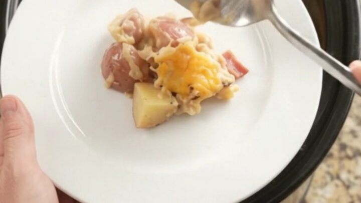 Slow cooker filled with cheesy red potato bake, golden crust and steam rising