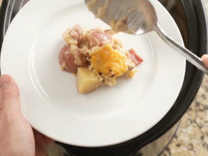 Slow cooker filled with cheesy red potato bake, golden crust and steam rising