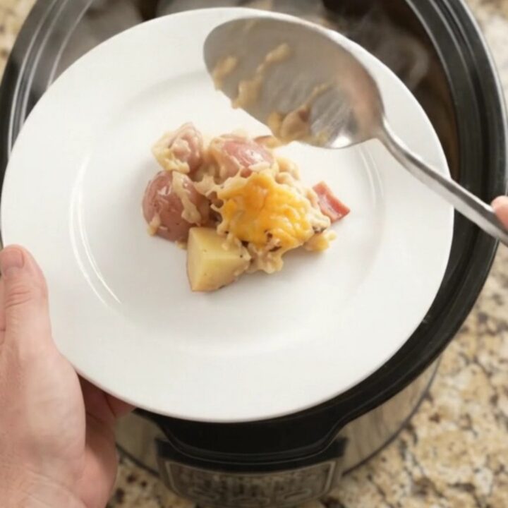 Slow cooker filled with cheesy red potato bake, golden crust and steam rising