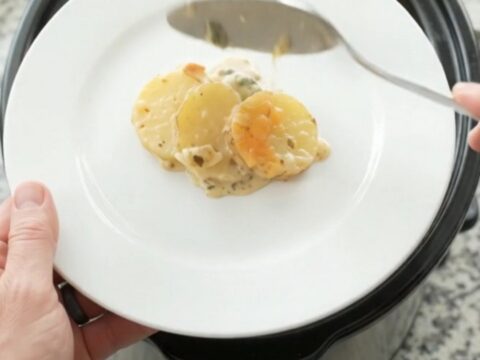 Slow cooker filled with bubbling scalloped potatoes topped with melted cheese