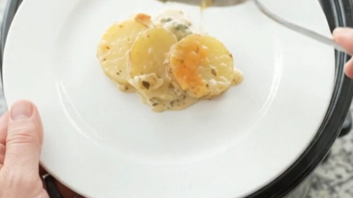 Slow cooker filled with bubbling scalloped potatoes topped with melted cheese