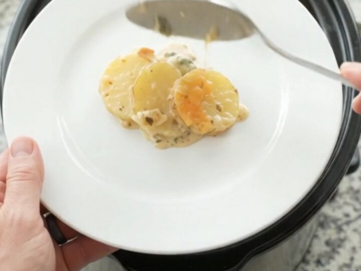 Slow cooker filled with bubbling scalloped potatoes topped with melted cheese