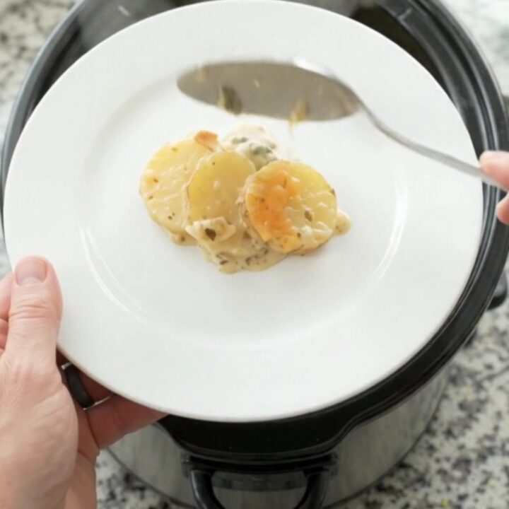 Slow cooker filled with bubbling scalloped potatoes topped with melted cheese